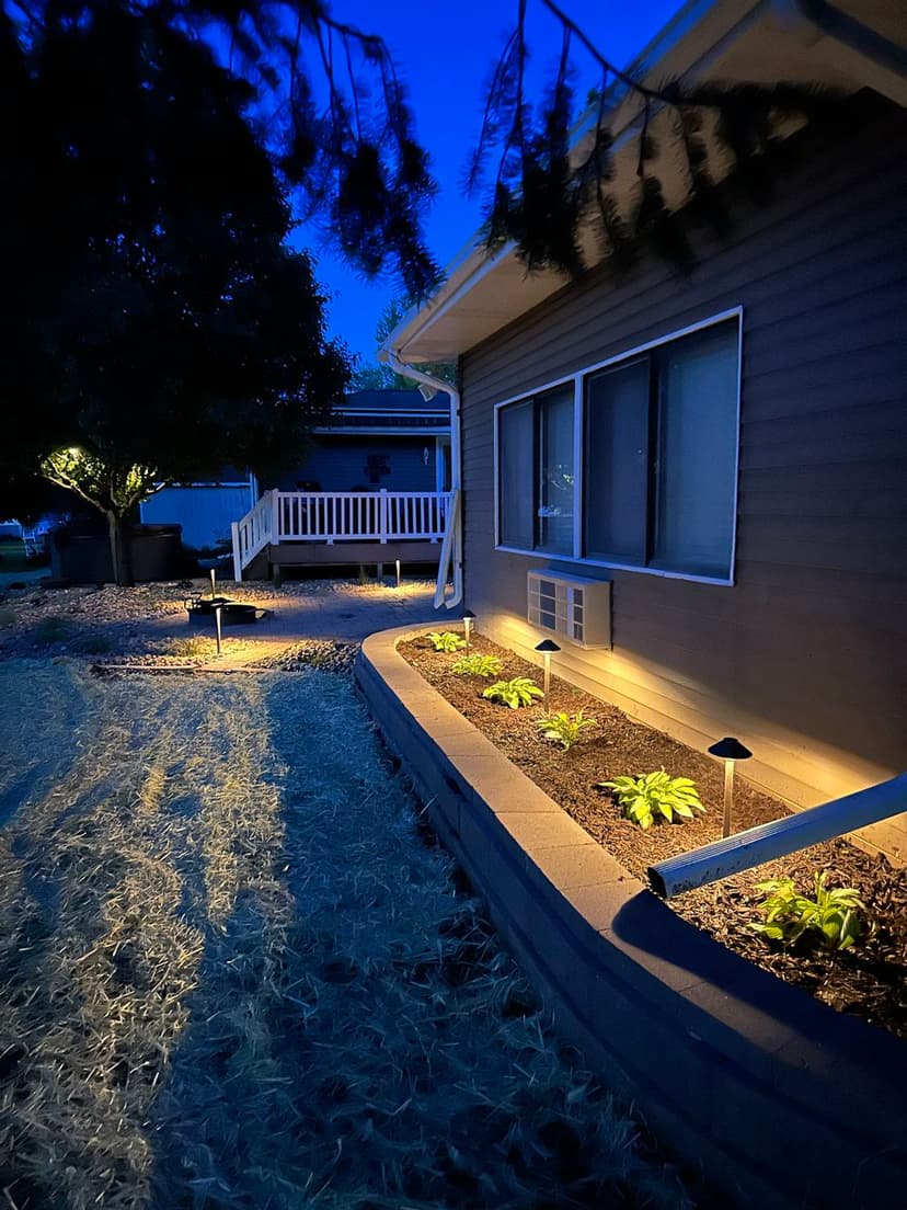 Nighttime landscape with illuminated garden beds beside a modern house.